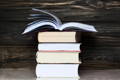 Stack of books with dark wooden background. One book is opened Stock Photos