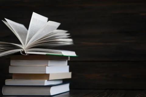 Stack of books with dark wooden background. One book is opened. Free space fo Stock Photos