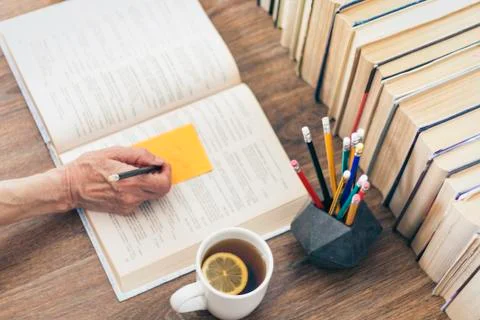 Stack of books education background, female hand makes notes near open textbo Stock Photos