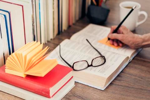 Stack of books education background, female hand makes notes near open textbo Stock Photos