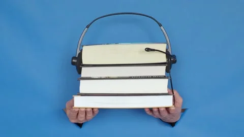 Stack of books in hands with headphones, audiobook concept, on a blue background Stock Footage 152731555