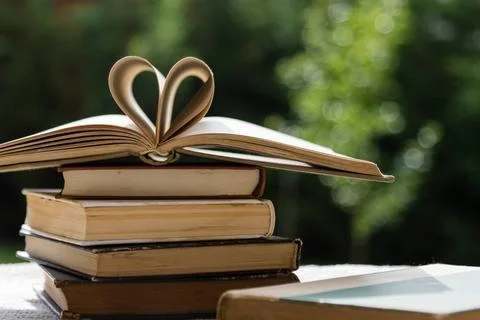 Stack of books with heart shape stack of books on table in garden with top... Stock Photos
