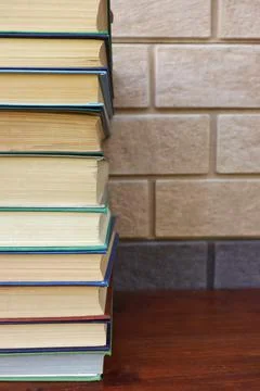 A stack of books lies on a wooden table against a brick wall Foto stock