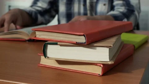 A stack of books lying on the desk of a reading man in the library Stock Footage 166361532