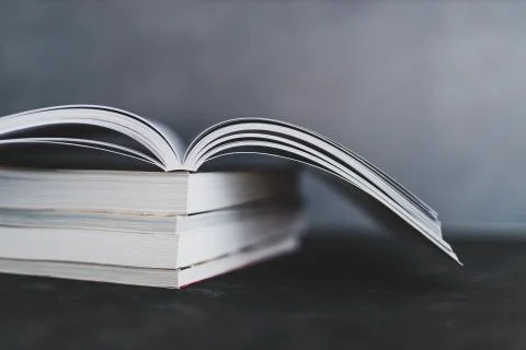 Stack of books with one open on top of them shot from eye level with shallow  Stock Photos