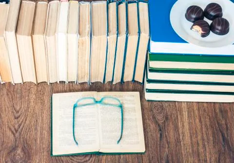Stack of books, open book, glasses and chocolate cookies white plate. Stock Photos