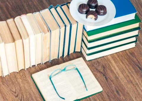 Stack of books, open book, glasses and chocolate cookies white plate. Stock Photos