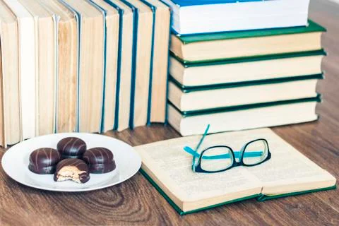 Stack of books, open book, glasses and chocolate cookies white plate. Stock Photos