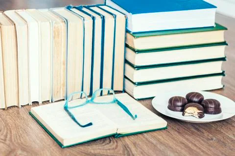 Stack of books, open book, glasses and chocolate cookies white plate. Stock Photos