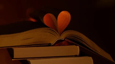 A stack of books with an open book on top. Creation the heart from book sheets Stock-Footage 72185347