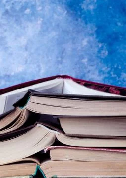 Stack of books piled against blue background. School concept. Stock Photos