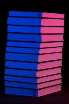 A stack of books in pink and blue light on a black background Фото
