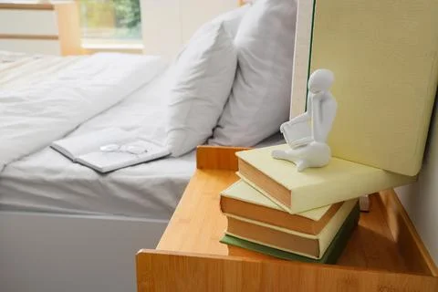 Stack of books with reading figurine on bedside table Stock Photos