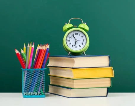Stack of books, a round alarm clock and multicolored pencils on the backgroun Stockfoto's