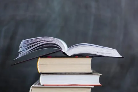 Stack of books with school chalkboard in background . One book is open Stock Photos