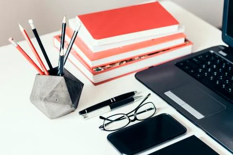 Stack of books, smartphone, laptop, glasses and pencils in holder, office bus Stock Photos