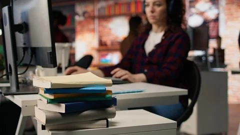 Stack of books on startup office desk in front of woman working, closeup 스톡 사진