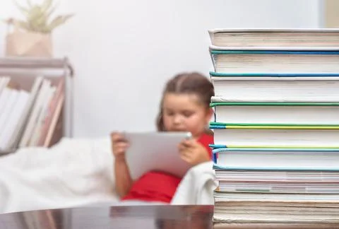 A stack of books on the table against the background of a child with tablet Stock Photos