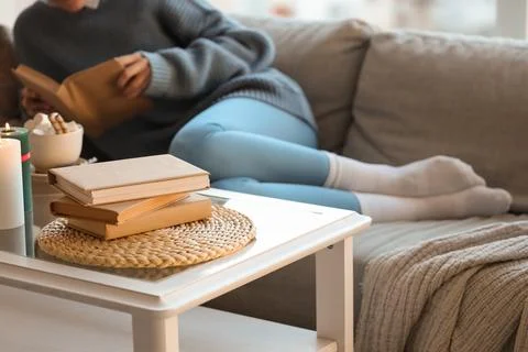 Stack of books on table against woman reading at home, closeup Stock Photos