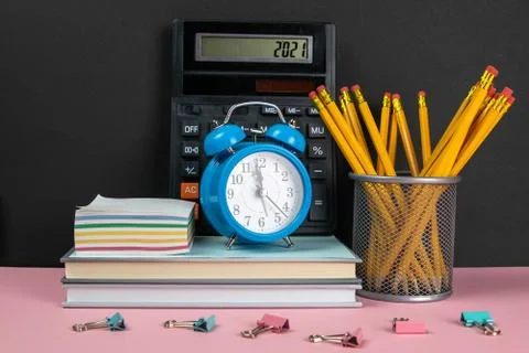 On a stack of books there is a calculator, a clock and sheets for notes, and  Stock Photos