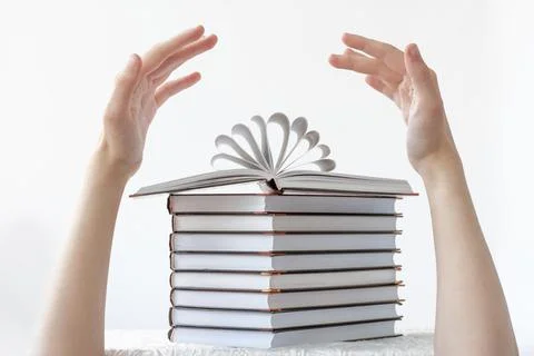 A stack of books on top of an open book and two hands over the books. The con Foto stock