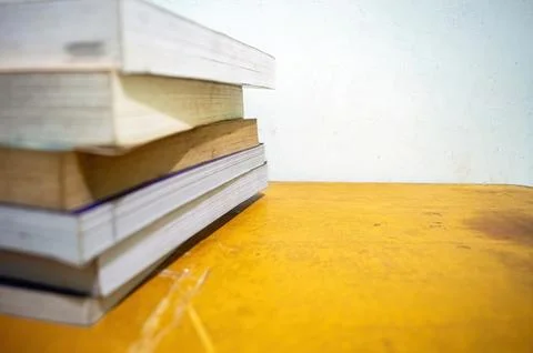 A stack of books on a yellow table against a plain white wall. The image hi.. Stock Photos