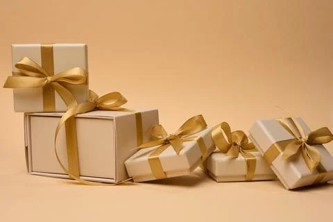 A stack of boxes tied with a golden ribbon on a beige background, festive b.. 库存照片
