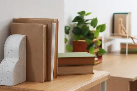 Stack of brown books with a modern white bookend on a wooden shelf in a home  Stock Photos