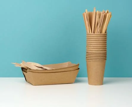 Stack of brown disposable paper cups on a white table, wooden forks and knive Stock Photos