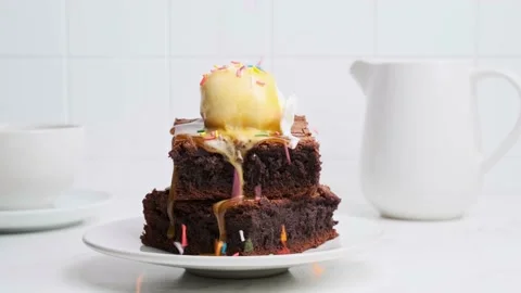 Stack of brownie squares with scoop of ice cream, colored sprinkles and caramel Stock Footage 166528020