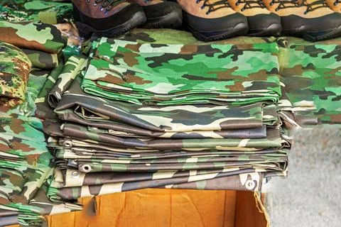 Stack of camouflage tarp covers boots and other hunting tools on market Stock Photos
