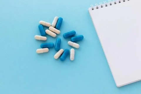 Stack of capsules and blank notepad isolated on light blue background. Legal Stock Photos
