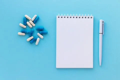 Stack of capsules, blank notepad and pen isolated on light blue background. L Stock Photos
