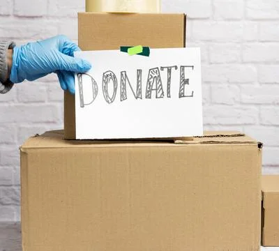 Stack of cardboard boxes and white sheet of paper with inscription donate Stock Photos