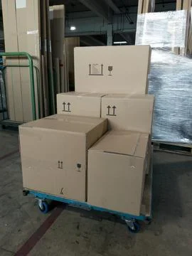 Stack of cardboard boxes on a blue dolly in a warehouse setting with wooden.. Stock Photos