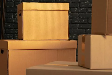 Stack of cardboard boxes in the empty room against black brick wall Stock Photos