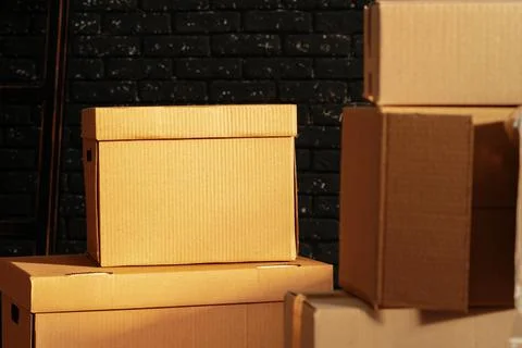 Stack of cardboard boxes in the empty room against black brick wall Stockfoto's