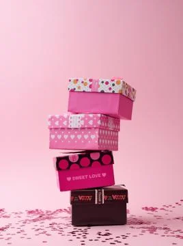 Stack of cardboard square gift boxes on a pink background with shiny confetti Stock Photos