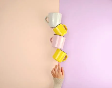 Stack ceramic cups are supported by a female hand on a beige lilac background Stock Photos