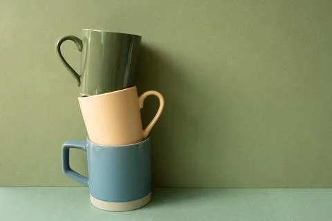 Stack of ceramic mug cups on green table. khaki wall background Stock Photos