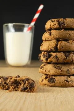A stack of chocolate chip cookies sits on a wooden table next to a glass of milk Stock Photos