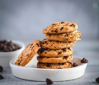 Stack of chocolate chip cookies on white plate and scattered chips Stock Photos