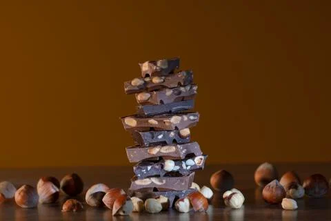 Stack of chocolate chunks surrounded by hazelnuts Stock Photos
