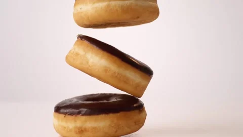 Stack of chocolate iced cake donuts bouncing on white slow motion macro food Stock Footage 336706691