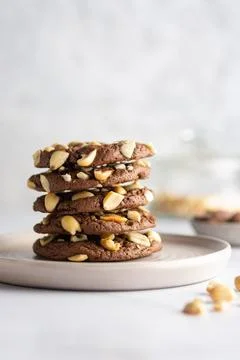 Stack of chocolate peanut cookies on a ceramic plate with blurred ingredients on Stock Photos