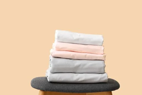 Stack of clean bed sheets on stool against beige wall Stock Photos