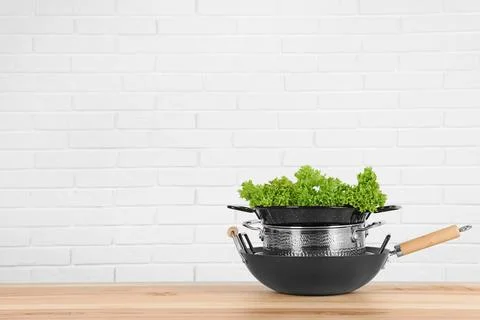 Stack of clean cookware with lettuce on table against white brick wall. Space Foto stock