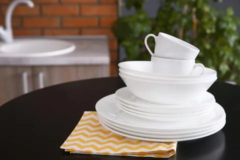Stack of clean dishes and cups on table against blurred background. Space for Stock Photos