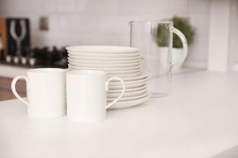 Stack of clean dishes, cups and glass jug on table in kitchen Stock Photos