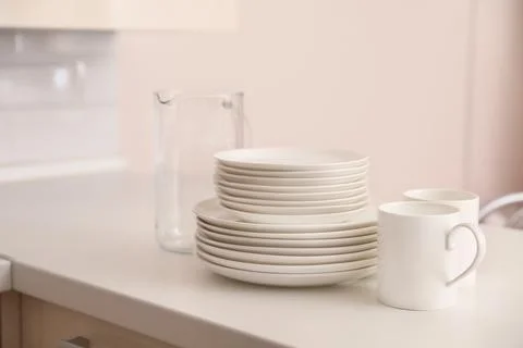 Stack of clean dishes, cups and glass jug on table in kitchen Stock Photos